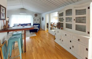 A spacious living area with a wooden floor, a dining table, blue chairs, a sofa, and a cabinet with glass doors. - 4 bedroom amazing home in Haverdal (Haverdal)