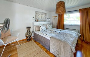 A bedroom with a bed, a standing fan, a decorative vase, a chair, and a window with curtains. - 4 bedroom amazing home in Haverdal (Haverdal)