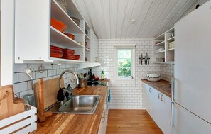 A compact kitchen with white cabinets, a wooden countertop, and a window providing a view of greenery outside. - 4 bedroom amazing home in Haverdal (Haverdal)