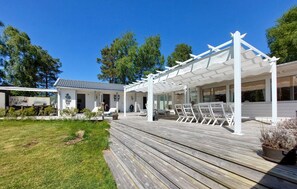 A wooden deck with outdoor seating, a covered patio area, and a house with a tiled roof. - 4 bedroom amazing home in Haverdal (Haverdal)