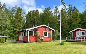 En röd stuga med en vit veranda, en satellitparabol och en flaggstång med en flagga.