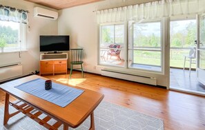 Ett rum med ett träbord, en tv, en stol och stora fönster med utsikt över grönområden.