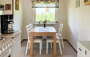 Una cocina con una mesa de madera, sillas blancas, una cafetera y una ventana con vistas a la vegetación.