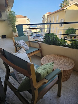 A balcony with wooden furniture, a round table, and a view of the street. - Walking Canes (Cannes)