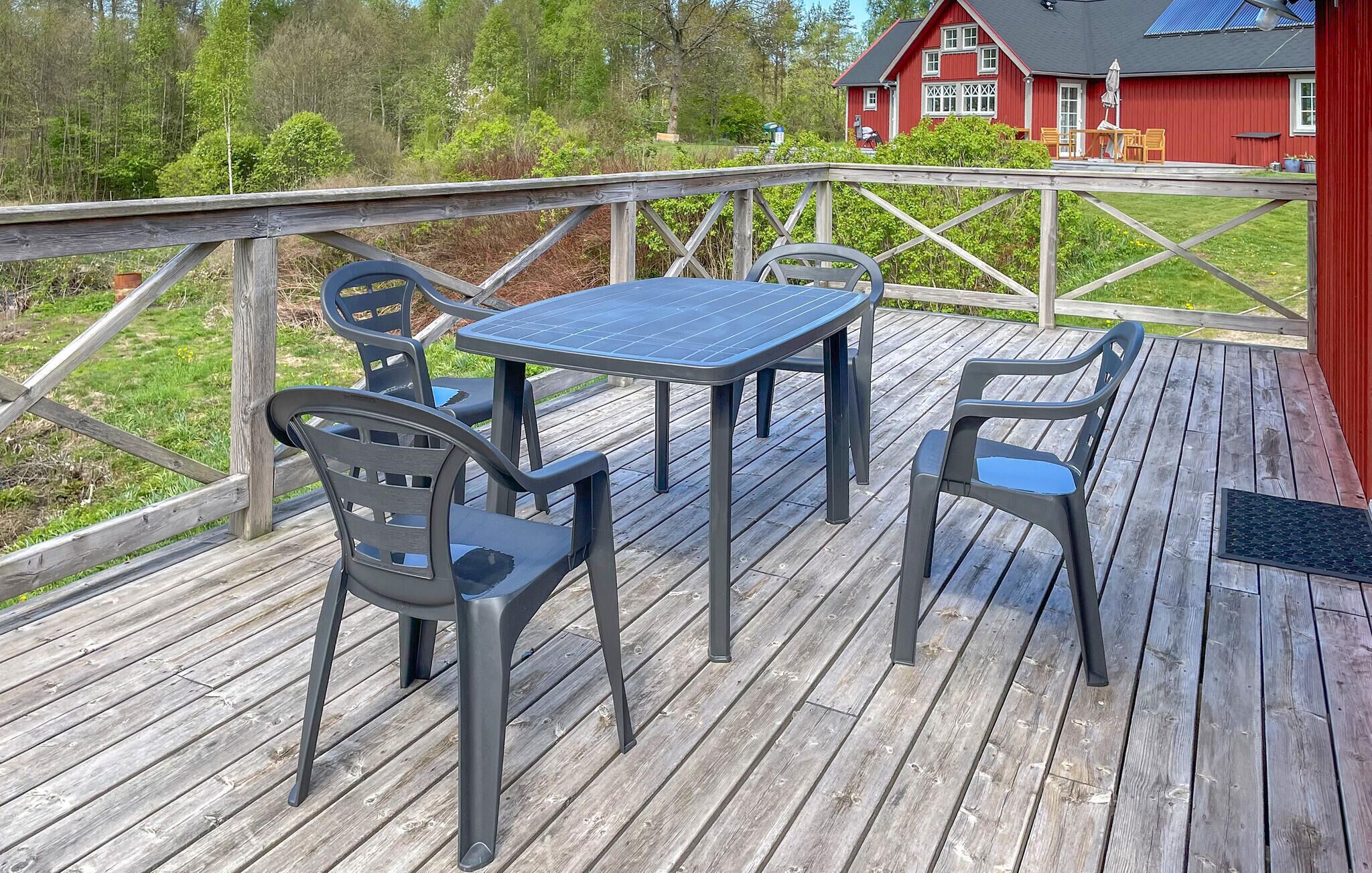 A wooden deck with a table and chairs, a red building in the background, and a grassy area.