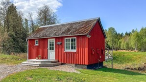 En rød træbygning med hvide døre og vinduer, omgivet af grøn vegetation og træer.