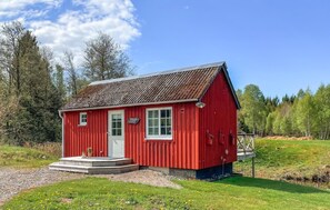 A red wooden building with a white door and windows, surrounded by greenery and trees.