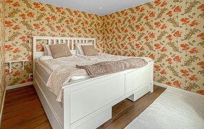 A white bed with a headboard, a bedside table, and a wall with floral wallpaper.