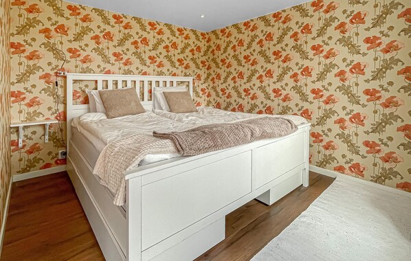 A white bed with a headboard, a bedside table, and a wall with floral wallpaper.