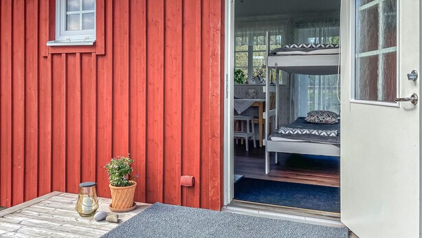 En rød træbygning med en dør, der fører til et rum med køjeseng og et bord med stole.