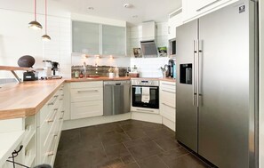 A modern kitchen with white cabinets, a stainless steel refrigerator, a dishwasher, and a built-in oven.
