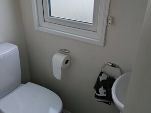 Uma casa de banho pequena com sanita, rolo de papel higiénico, um porta-toalhas com toalha e uma janela sobre a sanita.