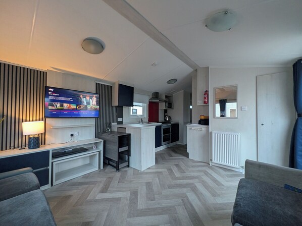Uma sala de estar moderna com televisão de tela plana, um sofá, cozinha com micro-ondas e área de refeições.