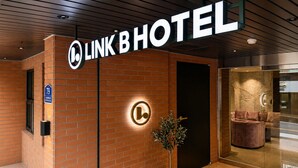A hotel entrance with a brick facade, a sign reading 'LINK B HOTEL,' and a potted plant. - Link B Hotel (Busan)