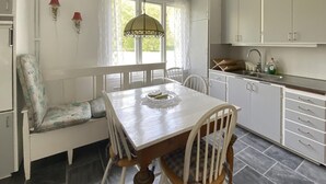 Un'area pranzo con tavolo in legno, sedie bianche, una panca e una finestra con lampadario.