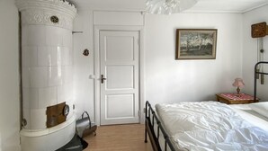 Una stanza con una porta bianca, un letto con biancheria da letto bianca, un quadro al muro e un pavimento in legno.