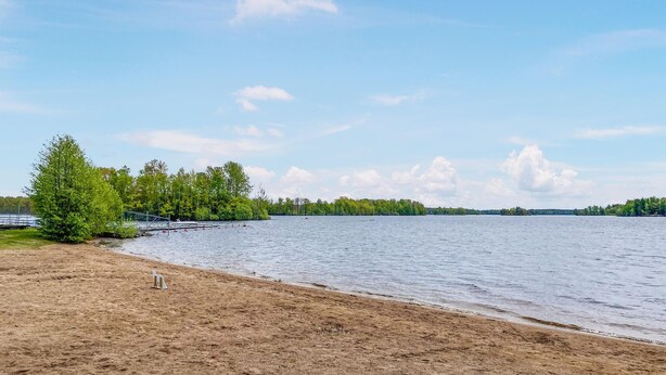 En strand med en sandstrand, en liten båt som ligger förtöjd och en skogbeklädd kustlinje.