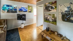 Ett vardagsrum med en tv, ett soffbord och tavlor på väggen som föreställer klassiska bilar och motorcyklar.