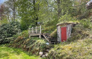 A rustic wooden staircase leading to a red door, surrounded by dense greenery and a thatched-roof structure. - Pet friendly home in Broaryd with WiFi (Broaryd)