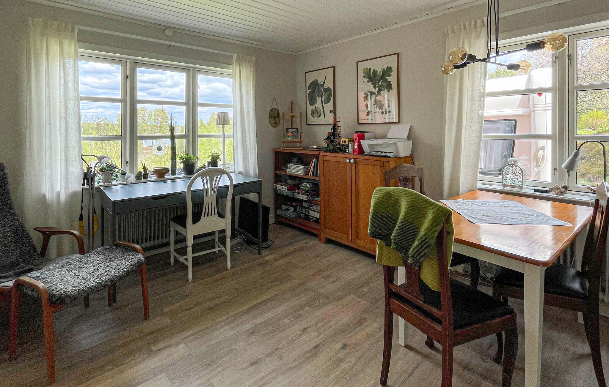 A room with a dining table, chairs, a radiator, a bookshelf, and large windows.