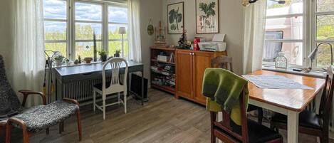 A room with a dining table, chairs, a radiator, a bookshelf, and large windows.