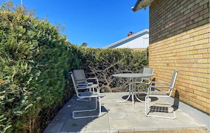 A patio with a table and chairs, a brick wall, and a hedge.
