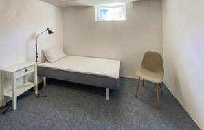 A small, single-bed room with a desk, chair, and a small window.