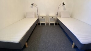Habitación doble con dos camas individuales, mesitas de noche, lámparas y piso alfombrado.