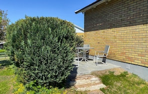 A patio with a table and chairs, a hedge, and a brick wall.