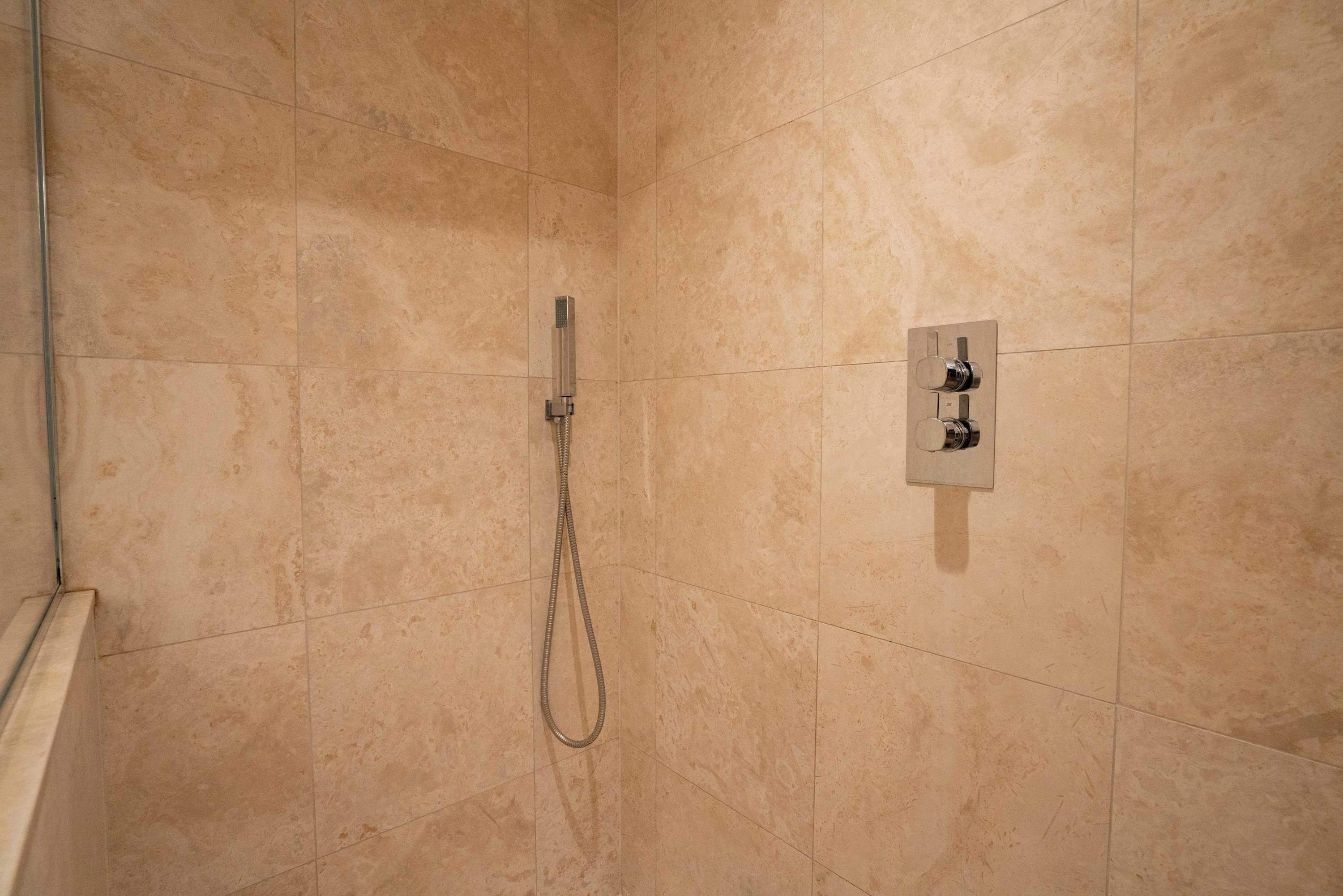 Een badkamer met beige tegels, een douchekop en bedieningspaneel.