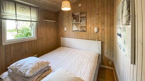 Una habitación con paneles de madera, una cama, un ventanal y una lámpara fijada a la pared.