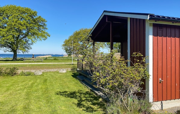 A red building with a porch, a grassy area, trees, and a view of the sea.