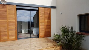 A modern building with a sliding glass door leading to a bedroom, a wooden deck, and a potted plant. - Asinerie Kuleni (Ponteilla)