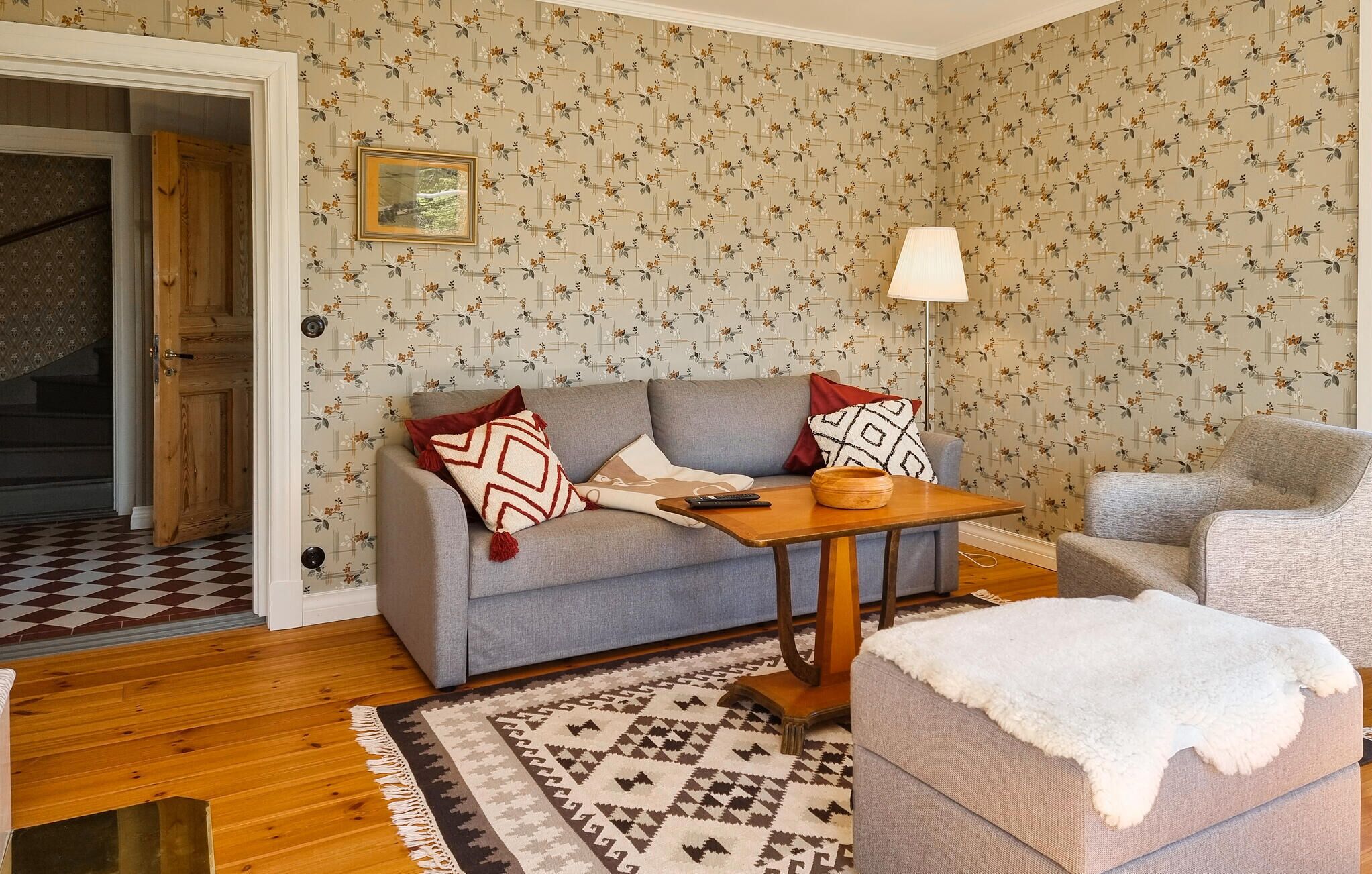 Un salón con sofá, una mesa, una lámpara y un papel tapiz estampado.