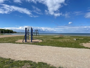 A playground with climbing structures and swings, a sandy area, and a body of water in the background. - Vacation Home "Sanddüne" – Apartment Luv (Right) in Zierow (Zierow)