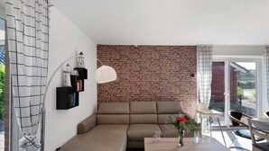 Uma sala de estar moderna com um sofá seccional, uma mesa de jantar com cadeiras, uma parede de tijolos e uma porta de vidro que dá para o exterior.