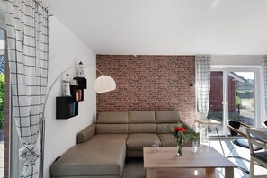 Ein modernes Wohnzimmer mit einer Eckcouch, einem Esstisch mit Stühlen, einer Ziegelwand und einer Glastür, die nach draußen führt.