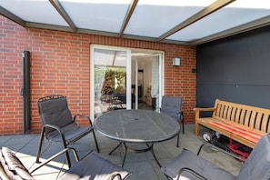 Eine Terrasse mit rundem Tisch und Stühlen, einer Holzbank und einer Ziegelwand.