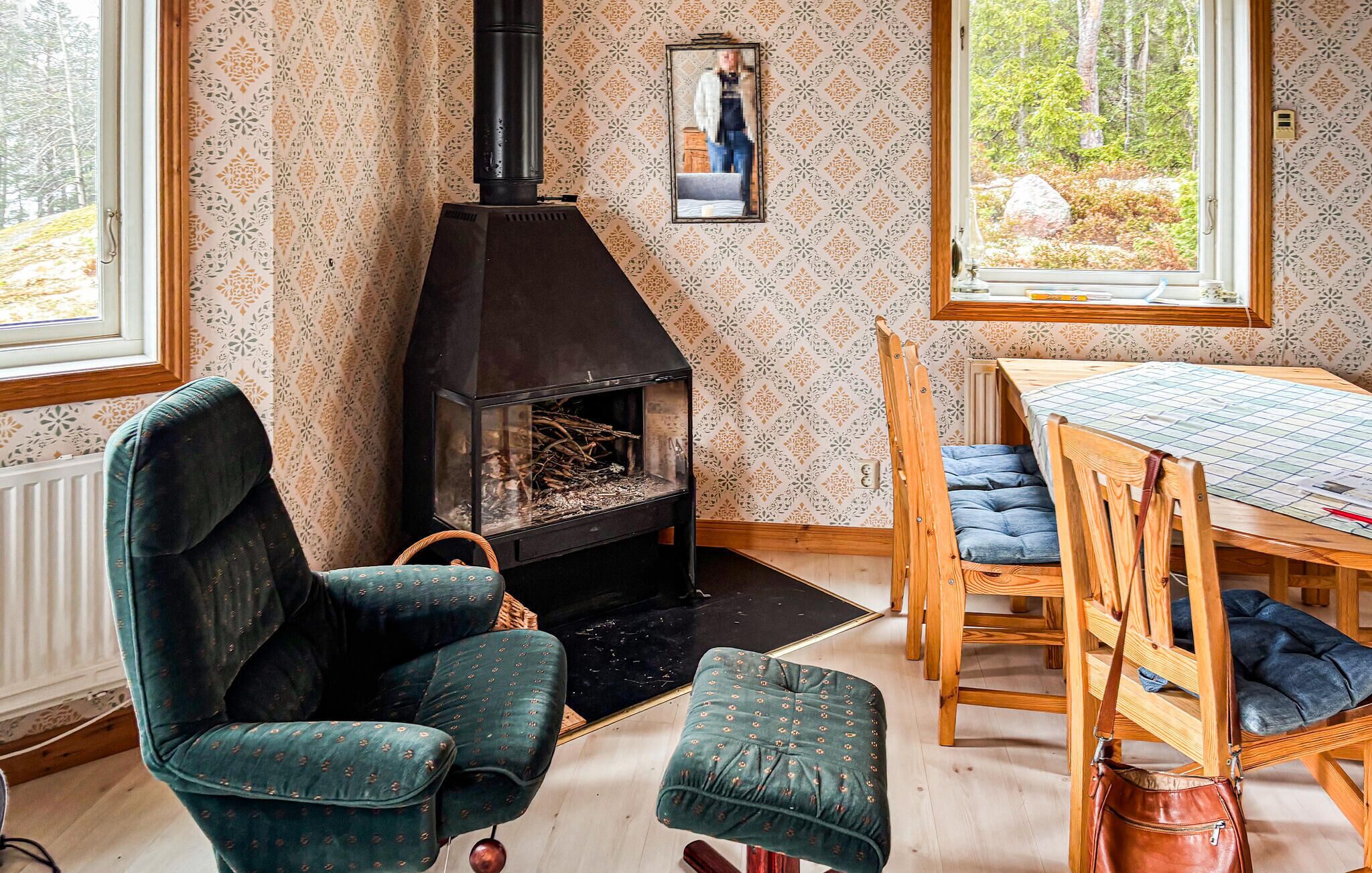 Une pièce chaleureuse avec une cheminée, un papier peint à motifs, une table à manger avec des chaises et une vue sur l’extérieur.