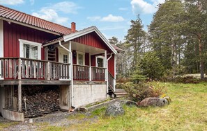 Ein rotes Holzhaus mit Veranda, Schornstein und Holzstapel davor.