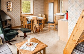 Ein gemütliches Zimmer mit Kamin, einem Esstisch mit Stühlen, einer Küchenzeile und einer Holztreppe.