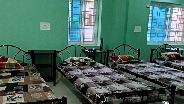 A room with three single beds, each with a patterned bedspread, a small bedside table, and a window with bars. - APARNA HOTEL DORMITORY (Bhubaneshwar)