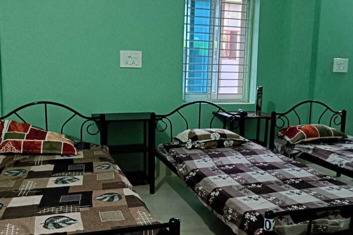 Una habitación con tres camas individuales, cada una con una colcha estampada, una mesita de noche pequeña y una ventana con rejas.