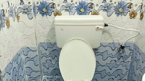 A bathroom with a toilet, blue patterned tiles, and a floral wallpaper design. - APARNA HOTEL DORMITORY (Bhubaneshwar)