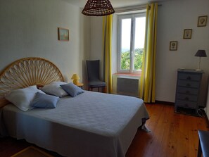 Una cama con cabecera, una silla, un aparador y una ventana con cortinas.