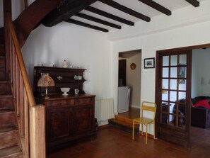 Una escalera de madera, un armario de madera con diversos objetos, un radiador, una silla y una puerta que da a otra habitación.