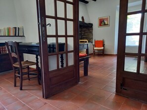 Una habitación con puerta de madera, un escritorio con libros, una silla, un banco y un cuadro en la pared.