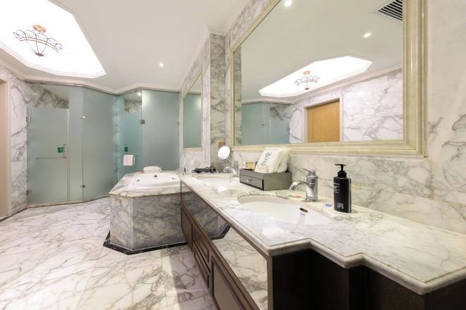A bathroom with marble flooring, a large mirror, a bathtub, and a double sink.