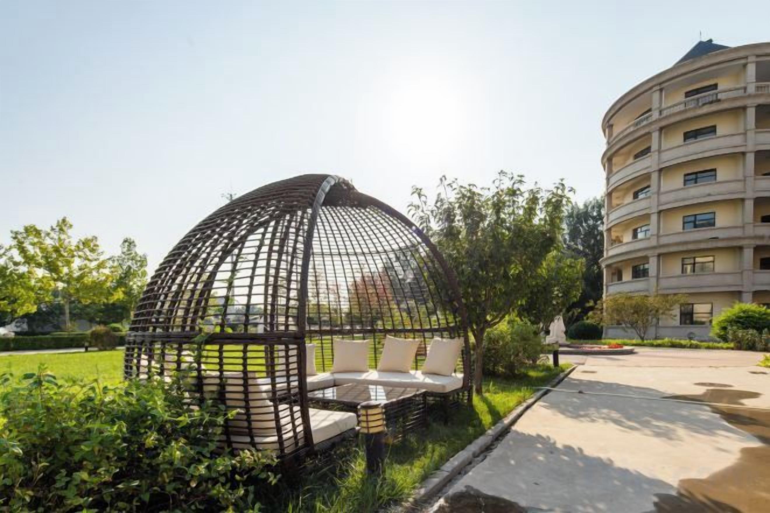 A spherical structure with seating, surrounded by greenery, next to a multi-story building.