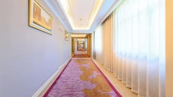 Een hotelgang met vloerbedekking, foto's in lijsten aan de muur en een raam met gordijnen.
